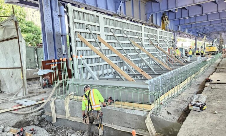 Construction workers in NYC install steel reinforcements and formwork for a concrete wall under a large, elevated bridge, advancing climate resilience through innovative techniques.