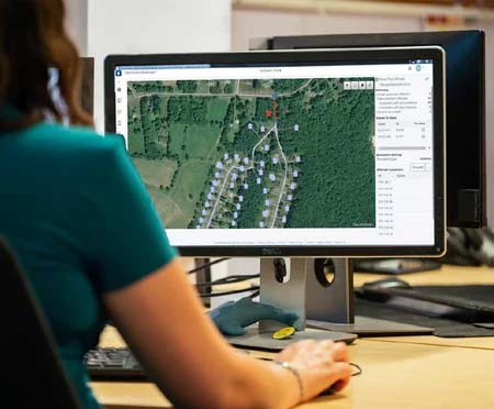 A person sits at a desk, using a computer displaying a satellite map with various marked points and details related to water infrastructure, expertly managed through MicroStation CAD. | Bentley Systems | Infrastructure Engineering Software Company A person sits at a desk, using a computer displaying a satellite map with various marked points and details related to water infrastructure, expertly managed through MicroStation CAD.
