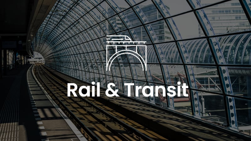 A graphic with the text "Rail & Transit" overlaid on an image of a modern train station, featuring curved glass walls and metal supports, powered by MicroStation technology.